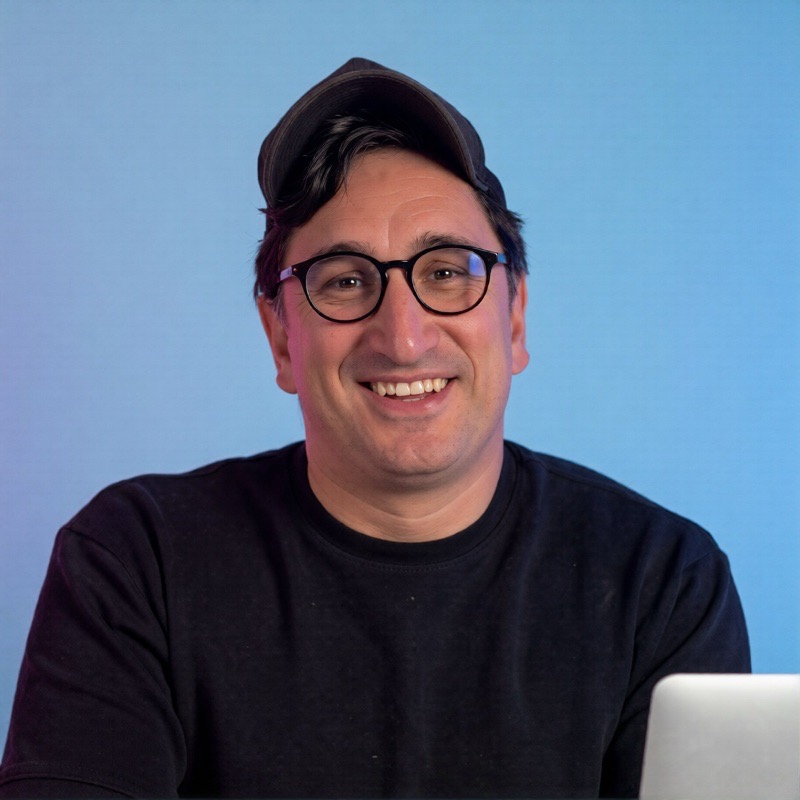 Nemanja Milic, wearing a cap and glasses, smiling at his desk.